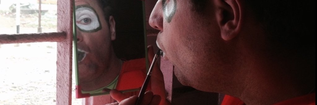 Clown sminkar sig och speglar sig i en handspegel
