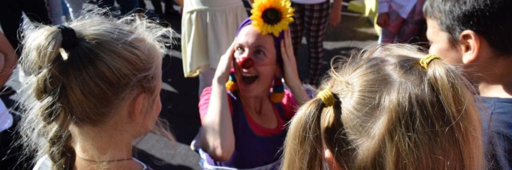 Skrattande clown med solros i håret omgiven av barn