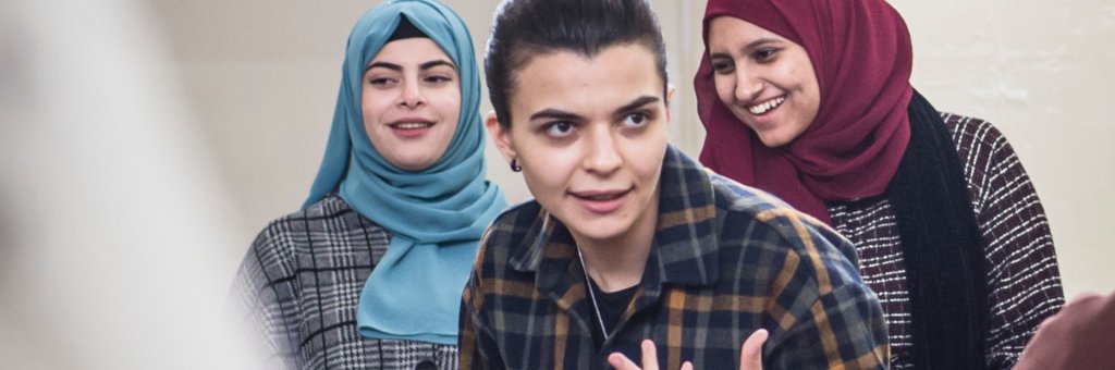 Ranin under en workshop, gestikulerar med händerna, i bakgrunden står två kvinnor i hijab och ler 