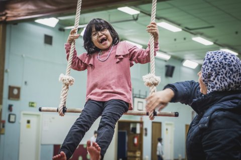 Ett barn sitter på en gunga och skrattar med sin mamma bredvid