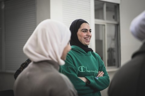 En kvinna i grön tröja och svart hijab som skrattar