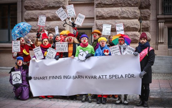 En samling clowner i färgglada skyltar och banderollen "Snart finns inga barn kvar att spela för"