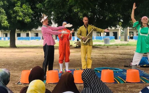 Fyra clowner i färgglada kläder uppträder för en grupp kvinnor i slöja