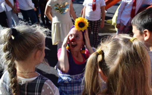 Skrattande clown med solros i håret omgiven av barn