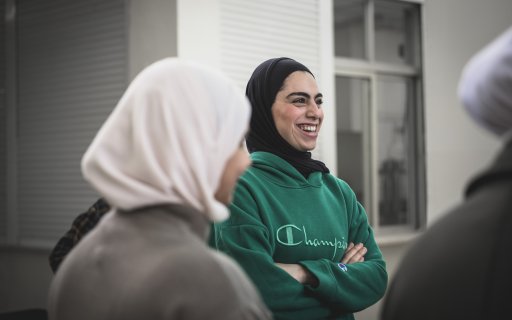 En tjej i hijab och grön tröja står och skrattar